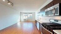 Located at 8310 N Interstate Ave in Portland, Oregon, this single-floor unit offers a thoughtfully designed open-concept layout with clean, modern finishes throughout. Rich wood-style flooring flows continuously across the living, dining, and kitchen areas, creating a warm and cohesive aesthetic.

The kitchen is a standout feature, equipped with dark espresso-toned cabinetry, white quartz countertops, stainless steel appliances including a gas range, built-in microwave, and dishwasher, as well as open floating shelves that add a contemporary touch. An exposed silver ductwork detail lends an industrial flair to the space.

The open living area is generously proportioned, bathed in natural light from large windows that frame outdoor views. Track lighting overhead adds both functionality and a modern design element. The layout flows seamlessly from the entry corridor into the main living space, providing a sense of openness and ease of movement.

The bathroom is finished with the same dark cabinetry and light countertop combination found in the kitchen, complemented by wood-style flooring, a full tub-shower combination, and a wide vanity mirror. The overall palette of white walls, warm wood tones, and dark accents gives the unit a clean, urban aesthetic well-suited to the Portland setting.