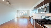 Located at 8310 N Interstate Ave in Portland, Oregon, this single-floor unit offers a thoughtfully designed open-concept layout with clean, modern finishes throughout. Rich wood-style flooring flows continuously across the living, dining, and kitchen areas, creating a warm and cohesive aesthetic.

The kitchen is a standout feature, equipped with dark espresso-toned cabinetry, white quartz countertops, stainless steel appliances including a gas range, built-in microwave, and dishwasher, as well as open floating shelves that add a contemporary touch. An exposed silver ductwork detail lends an industrial flair to the space.

The open living area is generously proportioned, bathed in natural light from large windows that frame outdoor views. Track lighting overhead adds both functionality and a modern design element. The layout flows seamlessly from the entry corridor into the main living space, providing a sense of openness and ease of movement.

The bathroom is finished with the same dark cabinetry and light countertop combination found in the kitchen, complemented by wood-style flooring, a full tub-shower combination, and a wide vanity mirror. The overall palette of white walls, warm wood tones, and dark accents gives the unit a clean, urban aesthetic well-suited to the Portland setting.