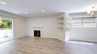 This single-floor unit offers a thoughtfully organized layout comprising a living room, kitchen, bedroom, bathroom, hallway, and closet. The living room serves as the focal point of the space, featuring a classic fireplace with a white surround and a built-in shelving unit along one wall, ideal for display or storage. Recessed lighting illuminates the room, complementing the light wood-tone laminate flooring that runs consistently throughout the unit. The open layout allows natural light to filter in, enhancing the clean, neutral color palette of white and soft gray tones on the walls.

The kitchen is designed in a galley configuration, outfitted with white shaker-style cabinetry, brushed nickel hardware, stainless steel countertops, and a full suite of appliances including a gas range, built-in microwave, dishwasher, and refrigerator. A window above the sink adds natural light to the workspace.

The bedroom is a well-sized room featuring recessed lighting, the same wood-tone flooring, and a mirrored sliding-door closet that enhances the sense of space. The bathroom includes a glass sliding-door walk-in shower with white tile surround and brushed nickel fixtures, paired with a clean, minimalist finish throughout.