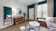 This well-designed one-bedroom, one-bathroom unit at 18590 E 61st Ave in Denver, Colorado offers a thoughtful layout with modern finishes throughout. The open-concept kitchen and living area serves as the heart of the home, featuring white shaker cabinets with black hardware, grey quartz countertops, a classic subway tile backsplash, and stainless steel appliances. A central island with seating and striking pendant lighting adds both function and style to the space. Wood-look flooring flows seamlessly throughout, creating a warm and cohesive aesthetic. The living room stands out with a bold deep teal accent wall, large windows that invite abundant natural light, and direct access to the entry door. The bedroom is a serene retreat finished in soft sage green tones, offering generous natural light through large windows, private outdoor access via a glass-paneled door, a ceiling fan, and a dedicated closet. The bathroom is clean and contemporary, showcasing a long white vanity with grey countertop, black hardware accents, wood-look tile flooring, and a full tub-shower combination. Every room reflects a cohesive modern design sensibility, making this unit a comfortable and stylish place to call home.