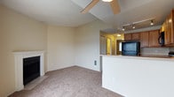 This single-floor residence offers a well-organized layout with a comfortable, functional design throughout. The living area serves as the heart of the space, highlighted by a classic white-mantled fireplace with a tile surround, providing a warm focal point. Plush wall-to-wall carpeting runs throughout the main living areas and bedroom, adding a cozy feel underfoot. A ceiling fan overhead aids in air circulation, while a sliding glass door connects the living room to an outdoor balcony, filling the space with natural light and views of the surrounding landscape.

The kitchen is positioned adjacent to the living area, separated by a convenient breakfast bar that creates an open yet defined boundary between the two spaces. Warm wood-toned cabinetry pairs with black appliances, including a refrigerator, range, and microwave, while track lighting above ensures ample illumination. The kitchen also features hard-surface flooring for easy maintenance.

The bedroom is a generously sized, quiet retreat featuring a large window fitted with blinds that invite natural light, a closet, and a baseboard heating unit. The bathroom is efficiently laid out with a combined tub and shower, wood-look flooring, a vanity with storage, and the added convenience of a stacked in-unit washer and dryer.