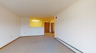 Located at 6160 Dell Dr in Madison, Wisconsin, this single-floor unit offers a practical and well-organized layout across its living spaces. The carpeted living room is generously sized, filled with natural light, and provides direct access to a private balcony through a sliding glass door, where a wall-mounted air conditioning unit also serves the space. A baseboard heating system runs along the perimeter, ensuring comfortable year-round temperatures. The kitchen is efficiently designed with white cabinetry, warm laminate countertops, a tile floor, a double sink, an electric range with overhead ventilation, and a full-size refrigerator. A pass-through counter connects the kitchen to the living area, creating an open and communicative flow between the two spaces. The bedroom features plush carpeting, ample wall space, and easy access to the rest of the unit. Two bathrooms serve the residence: a full bathroom equipped with a tub-shower combo, grab bars, a single vanity with under-sink storage, and a patterned tile floor, as well as a half bathroom featuring a single vanity and coordinating flooring. Throughout the unit, warm wood-toned door frames and trim provide cohesive architectural detail against the clean white walls.