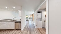 Located in Seattle's vibrant Wallingford neighborhood, Unit 102 at 4814 Interlake Ave N is a clean, modern single-floor residence featuring contemporary updates throughout. Light-toned luxury vinyl plank flooring runs continuously across the entire unit, lending a cohesive and polished feel to every room.

The galley-style kitchen is well-appointed with white shaker cabinetry, brushed hardware, quartz-style countertops, a stainless steel dishwasher, an electric range, and a full-size refrigerator — offering both style and functionality for everyday cooking.

A dedicated laundry closet houses a full stacked washer and dryer unit, providing the convenience of in-unit laundry. Adjacent to this is an additional utility or prep area with extra counter space.

The living area is bright and welcoming, with large windows and sliding glass doors that open directly to a private outdoor patio, allowing natural light to fill the space and providing a seamless indoor-outdoor connection to a landscaped exterior.

A standout architectural detail is the striking sliding partition door featuring a warm red-toned wood frame with frosted glass panels, offering a bold design accent while providing flexible room separation.

The bathroom is neatly finished with a single vanity, undermount sink, quartz countertop, a tub-shower combination, and wood-look flooring that ties in with the rest of the unit.