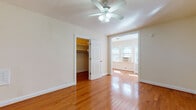 This single-floor residence offers a well-organized layout with a clean, neutral aesthetic throughout. The main living area is finished with rich, polished hardwood flooring that extends across multiple rooms, reflecting natural light and adding warmth to the space. A ceiling fan provides both light and airflow, enhancing everyday comfort.

The bedroom is generously proportioned and connects directly to a walk-in closet fitted with built-in shelving and hanging rods, offering ample storage. An open doorway leads to a bright sunroom or bonus room lined with windows, allowing abundant natural light to pour in and creating a versatile secondary space.

The kitchen is compact and efficiently designed, featuring white cabinetry, dark countertops, a subway tile backsplash, a gas range, and a stainless steel sink. A window above the counter brings in additional natural light, keeping the space feeling open despite its size. Light tile flooring completes the kitchen's clean look.

The bathroom showcases a classic black-and-white design with white subway wall tiles accented by black border tiles, a pedestal sink, and a full bathtub with an overhead shower. Diamond-patterned floor tiles add a timeless character to the room.

Additional storage is available through a dedicated walk-in closet with hardwood floors and multi-level shelving, making this space both practical and well-appointed throughout.