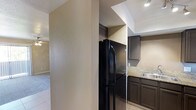 This single-floor space offers a practical and cohesive layout designed for comfortable everyday living. The kitchen is a standout area, showcasing dark espresso-toned cabinetry that provides ample storage, paired with light granite countertops that add a touch of elegance and contrast. A full-size black refrigerator anchors the space, complementing the dark cabinetry for a unified, modern aesthetic. A stainless steel sink is conveniently positioned along the counter, and recessed lighting illuminates the workspace effectively. The kitchen flows naturally into adjacent living areas, connected by a structural dividing wall that adds architectural definition to the layout. Light-toned tile flooring runs throughout, offering durability and easy maintenance, while the neutral beige walls provide a warm, understated backdrop. The textured wall finish adds subtle visual depth to the interior. The overall ambiance is clean, functional, and move-in ready, with a straightforward design that allows for easy personalization. The single-floor layout ensures seamless accessibility throughout the space, making it a practical and inviting environment.