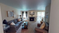 Located at 5617 111 St E in Puyallup, Washington, this single-floor residence offers a thoughtfully laid-out living space with a warm and inviting atmosphere. The living room serves as the heart of the home, centered around a classic fireplace with a white mantle and a wall-mounted television above. Plush carpeting, a large sectional sofa, and a chaise lounge create a comfortable gathering area, while a sliding glass door allows natural light to fill the room and provides access to an outdoor patio. The kitchen is well-appointed with rich, medium-toned cabinetry, stainless steel appliances including a range and refrigerator, and light hardwood flooring that adds warmth to the space. A dedicated dining area is conveniently adjacent. The home includes multiple bedrooms, each finished with soft carpet and neutral walls that lend a calm, restful ambiance. The primary bedroom features a built-in closet with sliding doors, offering ample storage. A secondary bedroom provides a charming, light-filled retreat with windows dressed in blinds. An additional smaller bedroom rounds out the sleeping accommodations. Throughout the home, the decor is cohesive and cottage-inspired, with soft color palettes and tasteful accents contributing to an overall sense of comfort and ease.