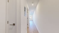 This thoughtfully renovated single-floor unit showcases a clean, contemporary design with light hardwood flooring and crisp white walls carried consistently throughout the space. The open-concept kitchen is a standout feature, outfitted with bright white shaker-style cabinetry, light stone countertops, and a full suite of stainless steel appliances including a refrigerator, range, built-in microwave, and dishwasher — all set against a subway tile backsplash. A pass-through window connects the kitchen area to an adjacent space, enhancing the open feel. The spacious living and dining area flows naturally from the kitchen, offering generous room to arrange furnishings with ease. Recessed lighting illuminates the interiors throughout. Bedrooms are bright and airy, benefiting from large double-hung windows that frame neighborhood views and invite abundant natural light. A lower-level room features a tray ceiling and a high transom window, offering a versatile additional space. The full bathroom is finished with large-format stone-look floor and wall tiles, a soaking tub with a combined shower, and a modern wood-toned vanity with a white countertop. A long hallway with recessed lighting connects the living spaces, with convenient built-in closets and utility access along the way.