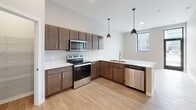 Located at 5571–5625 33rd Ave S in Fargo, North Dakota, this single-floor unit offers a clean, modern aesthetic with thoughtfully designed spaces and quality finishes throughout. The open-concept kitchen is a standout feature, showcasing rich dark-walnut cabinetry, crisp white quartz countertops, and a full suite of stainless steel appliances including an electric range, built-in microwave, and dishwasher. Stylish pendant lighting hangs above the extended kitchen peninsula, which flows seamlessly into the living and dining area. Light wood-look flooring runs throughout the main living spaces, adding warmth and continuity to the open layout. Natural light filters in through well-placed windows, enhancing the bright and airy atmosphere. The bedroom is generously proportioned, finished with plush carpet and framed by large black-trimmed windows that offer views of the surrounding neighborhood. An expansive walk-in closet with wire shelving and hanging rods provides ample storage. The bathroom is finished with matching dark cabinetry, a white quartz vanity, a large mirror with overhead lighting, and a tub-shower combination. The cohesive design palette of neutral tones and contemporary fixtures creates a polished, move-in-ready living environment.