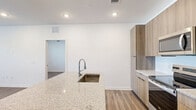 Located in Saint Augustine, FL, this well-appointed single-story residence offers two bedrooms and two bathrooms with a clean, modern aesthetic throughout. Wide-plank wood-look flooring runs consistently across all rooms, creating a cohesive and warm feel. The open-concept kitchen and living area serves as the heart of the home, anchored by a large island with granite countertops and an undermount sink. The kitchen is outfitted with flat-front wood-toned cabinetry, a white subway tile backsplash, and a full suite of stainless steel appliances, including a refrigerator with ice and water dispenser, electric range, built-in microwave, and dishwasher. Recessed lighting illuminates the space efficiently. The spacious primary bedroom features a ceiling fan, large windows with natural light, and access to an en-suite bathroom complete with a glass-enclosed walk-in shower, granite vanity, and wood-toned cabinetry. The second bedroom is bright and versatile, enhanced by dual windows fitted with white blinds. A dedicated closet with double panel doors adds practical storage. The second bathroom mirrors the same refined finishes, with a granite-top vanity and a shower enclosure. The overall design is clean, contemporary, and move-in ready.