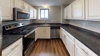 Located at 170 Washington in Haverhill, MA, this single-floor residence offers a thoughtfully designed layout with a clean, neutral aesthetic throughout. The kitchen is a standout feature, showcasing white shaker-style cabinetry, dark countertops, rich hardwood-style flooring, and stainless steel appliances including a dishwasher, microwave, and range — all anchored by a window that brings in natural light and exterior views. The open living area is generously sized, carpeted in warm beige tones, and lined with large floor-to-ceiling windows that frame sweeping panoramic views of the city skyline and surrounding waterway, flooding the space with natural light. The bedroom areas are comfortably proportioned, each featuring plush carpeting, closet storage, and windows that invite additional daylight. One bedroom benefits from direct access to a bathroom, offering added convenience. The bathroom is finished with wood-look flooring, a white vanity with sink, a tub-shower combination, and clean, understated fixtures. Neutral gray walls and white trim are consistent throughout, lending the space a cohesive and modern feel. The overall ambiance is bright, airy, and move-in ready, with scenic views serving as a defining and memorable characteristic of this Haverhill residence.