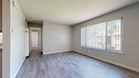 This single-story, one-bedroom, one-bathroom unit offers a clean and functional layout designed for comfortable everyday living. The living area is finished with light-toned laminate wood flooring, neutral gray walls, and a textured ceiling, creating a bright and welcoming atmosphere. A large window fitted with vertical blinds allows natural light to fill the space while offering outdoor views. A wall-mounted air conditioning unit provides climate control. The galley-style kitchen runs along two parallel walls, featuring gray cabinetry, warm granite-toned countertops, a gas range, refrigerator, over-range microwave, and a sink — all efficiently arranged to maximize workflow in a compact footprint. The bedroom is carpeted for comfort and includes a window with natural light, neutral walls, and a textured ceiling consistent with the rest of the unit. A dedicated walk-in closet off the bedroom provides dual hanging rods and carpeted flooring, offering generous storage. The bathroom is neatly appointed with a tiled tub-shower combination, wood-look flooring, and a vanity with a granite-toned countertop. Overall, the unit presents a cohesive, neutral aesthetic that is both practical and move-in ready.