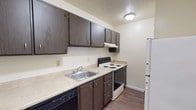Located at 20 Old Yellow Springs Road in Fairborn, Ohio, this single-floor unit offers a practical and straightforward layout suited for comfortable everyday living. The living area greets you at the front entry, where a paneled door with a transom window allows natural light to filter in. A ceiling fan overhead and a wall-mounted air conditioning unit ensure year-round comfort, while carpet flooring adds warmth underfoot. The open sightlines connect the living space to the rest of the unit, creating a cohesive flow throughout. The kitchen is a standout functional space, featuring dark wood cabinetry with ample upper and lower storage, light-toned countertops, a stainless steel sink, an electric range, a dishwasher, and a full-size refrigerator. Durable wood-look flooring runs through the kitchen, providing easy maintenance. Bedrooms are carpeted and well-proportioned, each equipped with ceiling fans or baseboard heating and windows dressed with blinds that allow for natural light and privacy. The bathroom is cleanly appointed with a full tub and shower combination, a toilet, a vanity with storage, and a medicine cabinet mirror. Neutral wall tones and consistent finishes throughout the unit contribute to a clean, move-in-ready atmosphere.
