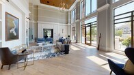 Located at 301 Newbrook Dr in Charleston, SC, this single-story clubhouse delivers an impressive blend of coastal charm and refined elegance. The grand main lounge commands attention with its soaring double-height ceilings, floor-to-ceiling windows, and wide-plank hardwood flooring that runs throughout the space. A statement chandelier anchors the room, while an abundance of natural light pours in through expansive glass doors that open to outdoor views of the surrounding landscape.

The lounge area features sophisticated coastal-inspired furnishings, including plush sofas and accent chairs in a palette of soft neutrals and blues, complemented by curated built-in shelving and coastal artwork. Adjacent seating nooks offer intimate spaces with bold navy wingback chairs set against classically paneled white walls.

A dedicated media lounge provides a comfortable gathering space with wall-mounted TV, navy upholstered seating, and steel-framed glass partition walls that maintain visual connectivity while offering separation. The corridor transitions seamlessly into a well-equipped kitchen and beverage station, distinguished by rich blue cabinetry, a geometric tile backsplash, warm wood ceiling accents, and a large island with butcher-block countertops and red upholstered bar seating. A dedicated refreshment bar with matching blue cabinetry, a round porthole window, and elegant elongated tile completes the space.