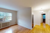 Located at 3 Manchester Place in Silver Spring, MD, this one-bedroom, one-bathroom unit offers a well-organized single-floor layout with warm hardwood flooring that flows seamlessly throughout every room. The combined living and dining area is bright and open, with natural light streaming through windows that offer views of mature trees. A radiator cover and window AC unit reflect classic building features, while a small chandelier adds a touch of elegance to the dining area. The kitchen is efficiently laid out and equipped with wood cabinetry and a stainless steel refrigerator. A hallway connects the main living spaces to the private bedroom, which benefits from two windows providing ample natural light and outdoor views, along with its own radiator and window AC unit. Two closets offer practical storage solutions. The bathroom features a timeless black-and-white tile design with a full soaking tub and shower combination, complemented by a small window for ventilation and natural light. Clean white walls throughout the unit create a neutral, versatile backdrop. Overall, the space presents a classic, functional design with consistent hardwood flooring and natural light as its defining characteristics.