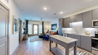 This well-designed one-bedroom, one-bathroom unit on N Oklahoma Ave in Oklahoma City offers a thoughtfully organized layout across a single floor. The open-concept living and kitchen area serves as the heart of the space, where wood-style flooring, recessed lighting, and a ceiling fan contribute to a clean, contemporary ambiance.

The kitchen is a standout feature, equipped with stainless steel appliances including a refrigerator, range, microwave, and dishwasher. Sleek gray cabinetry with under-cabinet lighting, white quartz countertops, a subway tile backsplash, and a freestanding island with a granite surface provide ample workspace and storage. The kitchen flows directly into the living area, which benefits from natural light through floor-to-ceiling glass doors opening to a balcony, framed by navy drape panels.

The bedroom accommodates a generous furniture arrangement and is brightened by large windows with blinds and drapes. It connects via a hallway to the bathroom, which features a granite-topped gray vanity, a glass-enclosed walk-in shower with tile surround, and matching overhead cabinetry for additional storage. Consistent wood-style flooring ties the entire unit together cohesively.