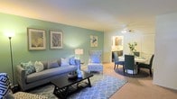 Located at 3004 Dorner Cir in Raleigh, NC, this single-floor residence offers a well-designed layout with a seamlessly connected living and dining area. The living room features a soft teal accent wall that adds a pop of color, complemented by warm neutral tones on the surrounding walls and plush carpeted flooring. A ceiling fan provides comfort overhead, while a stylish floor lamp contributes to the warm lighting throughout the space. The living area is thoughtfully arranged with ample seating and a central coffee table, creating an inviting atmosphere for both relaxation and entertaining. Adjacent to the living space, the dining area accommodates a full table and chairs set, anchored by a coordinating area rug. The open sightline between the two areas enhances the sense of spaciousness and flow. A glimpse into the background reveals a kitchen or utility area with cabinetry and countertops, adding to the functional layout of the home. The cohesive color palette of blues and greens carried throughout the furnishings and décor ties the space together with a calm, modern aesthetic. Overall, this residence offers a comfortable and practical single-level living experience in a well-established Raleigh neighborhood.