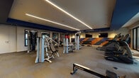 Located in Denver, CO, this modern fitness center offers a comprehensive, well-appointed space designed for a full range of workout activities. The main gym area is outfitted with professional-grade equipment, including True treadmills, StairMaster steppers, rowing machines, ellipticals, and a robust selection of strength-training machines from brands such as Hoist and RAX. A dedicated free weights section features an organized dumbbell rack alongside medicine balls and kettlebells, complemented by a bold geometric accent wall in navy, orange, and black that adds an energetic visual element to the space. Linear LED lighting runs along the ceiling, delivering bright, even illumination throughout. Large floor-to-ceiling windows flood the cardio area with natural light and open views of a connected outdoor terrace, creating an airy, inviting atmosphere. A built-in shelving and refreshment station is conveniently positioned nearby. Adjacent to the main gym, a separate studio room features light hardwood flooring, a tray ceiling with ambient lighting, wall-mounted mirrors, a ballet barre, and a mounted flat-screen display—ideal for group classes, yoga, stretching, or personal training sessions. The overall design balances functionality with a polished, contemporary aesthetic suited for serious fitness enthusiasts.