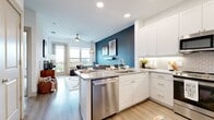 This thoughtfully designed one-bedroom, one-bathroom residence offers an efficient and stylish single-floor layout. The open-concept kitchen flows seamlessly into the living area, featuring white shaker cabinetry, a subway tile backsplash, granite countertops, stainless steel appliances including a dishwasher, and a pendant light above the peninsula — ideal for both cooking and casual dining. A bold teal accent wall adds a striking visual anchor between the kitchen and living space.

The living room is bright and inviting, bathed in natural light from large windows and a glass balcony door that opens to outdoor views of the surrounding cityscape. Light wood-look flooring runs throughout the main living areas, complementing the warm, contemporary aesthetic. A ceiling fan adds comfort overhead.

The entry area features a built-in mudroom nook with upper cabinetry, a granite bench, and coat hooks, alongside a double-door closet for generous storage.

The bedroom is a serene retreat with plush carpeting, dual windows offering scenic views, a soft accent wall, and a ceiling fan. The bathroom is well-appointed with a granite vanity, white cabinetry, wood-look flooring, and a tub-shower combination with marble-style tile surround. A walk-in closet connects directly to the bathroom for added convenience.