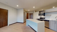 Located at 9150 W Watertown Plank Rd in Wauwatosa, Wisconsin, this single-floor unit offers a thoughtfully designed, contemporary living space. The open-concept layout seamlessly connects the kitchen and living area, creating a bright and airy atmosphere enhanced by recessed lighting and light-toned luxury vinyl plank flooring throughout.

The kitchen is well-appointed with a full suite of stainless steel appliances, including a refrigerator, electric range, over-the-range microwave, and dishwasher. Light wood-toned cabinetry pairs with clean white countertops on the central island, which provides additional prep and storage space. A wall-mounted mini-split HVAC unit ensures personalized climate control in the main living area.

Large sliding glass doors in the living space open to a private balcony, inviting abundant natural light and outdoor views into the interior. The bedroom is a comfortable retreat, finished with plush carpet and featuring a sliding door closet with built-in shelving. A wall-mounted mini-split unit also serves this room for year-round comfort.

The bathroom showcases a wide vanity with a white countertop, undermount sink, and light wood cabinetry with brushed nickel hardware. A large mirror reflects the clean, modern aesthetic. Conveniently, an in-unit stacked washer and dryer is also accessible, adding practical everyday functionality to this well-designed space.