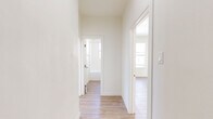 Located at 3333 W 4th St in Los Angeles, this well-appointed one-bedroom, one-bathroom unit offers a clean, modern aesthetic throughout. Light wood-style flooring runs continuously across all rooms, creating a cohesive and airy feel. The galley-style kitchen is thoughtfully designed with white shaker cabinetry, sleek quartz countertops, a stainless steel gas range, and a full-size stainless steel refrigerator. A charming arched window allows natural light to fill the kitchen space. The living area is open and bright, benefiting from large windows that frame city views of the surrounding Los Angeles skyline and neighboring architecture. The spacious bedroom is bathed in natural light from dual windows offering elevated urban vistas, giving the room a comfortable and inviting atmosphere. A compact radiator adds a classic touch. The bathroom is finished in crisp white tiling with a soaking tub, a rainfall showerhead with brushed gold fixtures, a white vanity with quartz countertop, and a small window for ventilation and light. A connecting hallway provides a smooth flow between all rooms. The overall design is clean, neutral, and modern, making this unit a bright and functional urban retreat in the heart of Los Angeles.