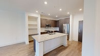 Located at 350 Village Dr in King of Prussia, PA, this well-appointed one-bedroom residence offers a thoughtfully designed single-floor layout that maximizes both functionality and comfort. The open-concept kitchen and living area serves as the heart of the home, highlighted by a prominent granite-topped island with an integrated sink — ideal for both meal prep and casual dining. The kitchen is outfitted with sleek, dark wood-grain cabinetry, a stainless steel refrigerator, range, and built-in microwave, all complemented by crisp white countertops and recessed lighting overhead. Light wood-style flooring flows throughout the main living area, lending warmth and continuity to the space. Large windows in the living room invite generous natural light while offering views of the surrounding community. The bedroom is carpeted for comfort, features a ceiling fan, a walk-in closet with wire shelving, and a window with outdoor views, creating a serene retreat. A dedicated laundry room houses a full-size Whirlpool front-loading washer and dryer set, adding everyday convenience. Clean white walls, modern finishes, and a neutral palette throughout give the space a fresh, contemporary feel.