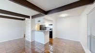 This single-floor residence offers three bedrooms and three bathrooms within a well-organized layout. The combined living and dining area serves as the heart of the home, anchored by a striking full-height brick fireplace with a black hearth surround. Distinctive dark-stained exposed beam ceilings add architectural character, while large windows invite natural light and outdoor views. Rich terracotta tile flooring flows throughout the common areas, adding warmth and texture underfoot.

The kitchen is efficiently designed with white cabinetry, granite-style countertops, a double sink, and black appliances including a refrigerator and electric range. A peninsula with a breakfast bar connects the kitchen to the living area, creating an open and social atmosphere. Built-in open shelving provides additional storage and display space near the entrance.

The three bedrooms are carpeted and feature neutral white walls, windows with blinds, and ceiling fans for comfort. The primary bedroom is generously proportioned, offering ample space for furnishings. The bathrooms are finished with white tile flooring, vanities with gray countertops, and sliding closet doors, providing clean and functional spaces. A hallway connects the private areas of the home, contributing to a logical and easy-to-navigate floor plan throughout.