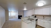 This single-story, two-bedroom, one-bathroom residence at Sapphire Creek offers an open and functional layout designed for comfortable everyday living. The kitchen serves as a central hub of the home, featuring white cabinetry, light granite-style countertops, a double-basin stainless steel sink, and a dishwasher. A peninsula counter connects the kitchen to the living area, creating a seamless flow ideal for both cooking and entertaining.

The living room extends generously from the kitchen and is anchored by a classic fireplace, adding warmth and a welcoming focal point to the space. Neutral-toned carpet covers the living area, complementing the light hardwood-style flooring in the kitchen. A window at the far end of the living room allows natural light to filter into the space. The overall color palette—white walls, light cabinetry, and soft flooring—creates a clean, bright ambiance throughout. Ceiling-mounted light fixtures provide consistent illumination, and a visible HVAC vent ensures year-round climate comfort. The unit's single-floor design offers easy accessibility and a cohesive living experience.