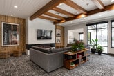 This thoughtfully designed single-floor amenity facility offers a comprehensive suite of spaces built for both relaxation and active living. The grand entrance lobby sets the tone with soaring ceilings, dramatic floor-to-ceiling black-framed windows, wide-plank light wood flooring, and striking woven pendant light fixtures that fill the space with an airy, welcoming atmosphere. Natural light pours in generously, offering views of the surrounding outdoor areas.

The lounge area features exposed wood beam ceilings with shiplap detailing, plush seating arrangements, and abundant windows that create a bright and sociable gathering space. A built-in window bench with colorful accent cushions serves as a cozy nook connecting the corridor to the lounge.

The fitness center is expansive and well-lit, boasting a vaulted ceiling, large black-framed windows with garden views, light wood flooring, and a full array of cardio and strength equipment. An adjoining room provides additional workout options.

The game room offers a lively atmosphere with a foosball table, bar-height seating, bold artwork, and a stylish wet bar backed by a geometric tile accent wall. A fully equipped kitchenette features stone countertops, dark cabinetry, stainless steel appliances, and a window overlooking a pool. An indoor pool area, accessible through glass-paneled doors, completes this exceptional amenity offering.