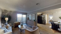 This single-floor residence offers a cohesive and thoughtfully designed layout across its key living spaces. The living room serves as the heart of the home, finished with warm neutral-toned walls, crown molding, and a textured ceiling. Large sliding glass doors fitted with vertical blinds open directly onto a private patio, allowing natural light to fill the room. The open sightline into the kitchen creates a connected, airy feel throughout the main area.

The galley-style kitchen is both functional and stylish, featuring dark espresso cabinetry paired with crisp light countertops, black appliances including a full-size refrigerator and range, and wood-look flooring underfoot. A window at the far end brings in additional natural light. Adjacent to the main living area, a dedicated dining nook provides an intimate space for meals, complete with a round table and structured seating beneath soft overhead lighting.

The bedroom is generously proportioned, offering plush carpeting, warm neutral walls, and a window with outdoor views. A connecting doorway leads conveniently to the full bathroom, which features wood-look flooring, a shower-tub combination, and clean, simple finishes throughout. The overall ambiance of the space is calm, modern, and move-in ready.