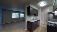 This single-floor unit offers a functional and well-appointed layout designed for comfortable everyday living. The open-concept design connects the kitchen directly to the living area, creating a seamless flow throughout the main living space. The kitchen is outfitted with dark espresso cabinetry, light countertops, a stainless steel sink, a dishwasher, and a range with an overhead exhaust hood. Wood-look flooring runs through the kitchen, providing a warm contrast to the darker cabinetry. The living area features neutral carpet, soft grey walls, and a textured ceiling. Large windows fitted with horizontal blinds allow natural light to fill the space while offering views of the surrounding neighborhood. A ceiling fan adds both function and style to the dining area adjacent to the kitchen. The bedroom is generously sized with plush carpeting, a sliding glass door opening to a private balcony, and a built-in closet with sliding panel doors. The bathroom is clean and bright, featuring wood-look flooring, a dark vanity with a light countertop, a toilet, and a full tub-shower combination with white surround. Baseboard heating is present throughout, and the textured ceilings are consistent across the unit, contributing to a cohesive interior aesthetic.
