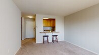 Located at 2746 Belmont Ave in Philadelphia's 19131 zip code, this two-bedroom, one-bathroom residence offers a practical and well-organized single-floor layout. The open living area features neutral-toned carpeting and receives natural light through a large window fitted with vertical blinds, creating a bright and airy atmosphere. A standout feature of the living space is the pass-through kitchen window with a granite-topped breakfast bar and two bar stools, blending the kitchen and living areas seamlessly. The kitchen is equipped with warm honey-toned wood cabinetry, granite countertops, a gas range, built-in microwave, refrigerator, and a sink — all set on light hardwood-style flooring. The two bedrooms are carpeted and offer comfortable proportions, with the primary bedroom providing a generous closet with built-in shelving and hanging rod. The bathroom features marble-look tile flooring, a full soaking tub with white subway tile surround, and a clean, functional design. A hallway connects all rooms efficiently, with additional closet storage accessible off the main corridor. The unit's straightforward layout and well-maintained finishes make it a practical and comfortable residence.