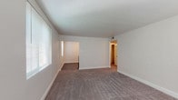This single-floor residence offers a clean, functional layout with a neutral color palette throughout, creating a bright and welcoming atmosphere. The living area is generously proportioned, featuring soft wall-to-wall carpeting, crisp white baseboards, and a windowed wall fitted with blinds that allows ample natural light to fill the space. An open pass-through connects the living area to an adjoining room, enhancing the sense of flow and connectivity.

The kitchen is well-equipped with white shaker-style cabinetry, dark countertops, and a contrasting tile backsplash. It features a full suite of black appliances, including a gas range, refrigerator, and overhead ventilation hood, all set on durable wood-look vinyl flooring that adds warmth and easy maintenance to the space.

The bedrooms are comfortably sized, each finished with plush carpeting and multiple windows dressed with blinds, ensuring both natural light and privacy. One bedroom includes a six-panel closet door and connects conveniently to adjacent spaces.

The bathroom is finished in clean white tile and features a full soaking tub and shower combination, with a window above providing ventilation and natural light. Wood-look flooring ties the bathroom's aesthetic to the rest of the home. Throughout, the space presents a tidy, move-in-ready condition with a consistent, understated design sensibility.
