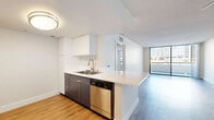 Located in the heart of downtown San Diego, this well-appointed one-bedroom, one-bathroom residence offers a thoughtfully designed layout with modern finishes throughout. Light wood-tone flooring flows seamlessly across the entire unit, creating a cohesive and contemporary aesthetic.

The combined kitchen and living area forms the centerpiece of the home. The kitchen features a peninsula with a white quartz countertop, a stainless steel sink, dark wood cabinetry, and a full suite of stainless steel appliances including a range, microwave, dishwasher, and refrigerator. The adjacent living area is bright and open, anchored by expansive floor-to-ceiling sliding glass doors that lead to a balcony and frame dynamic views of the San Diego skyline.

The bedroom is a well-sized retreat with large corner windows that bring in generous natural light and offer additional urban views. A mirrored sliding-door closet with built-in shelving provides ample storage. The bathroom continues the clean, modern design with dark wood vanity cabinetry, white quartz countertops, recessed lighting, and wood-look flooring. A hallway connects the main living spaces, completing this efficient and stylish urban residence.