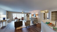 This single-floor residence offers a thoughtfully designed open-concept layout that connects the main living area, kitchen, and additional spaces with ease. The expansive living room features rich hardwood-style flooring, a ceiling fan, and a large window bay that fills the space with natural light. A decorative accent wall and wall-mounted television add character, while the open sightlines create a welcoming, airy atmosphere throughout.

The kitchen is outfitted with white shaker cabinetry, granite countertops, and stainless steel appliances including a refrigerator, range, and microwave. A peninsula counter connects the kitchen to the main living area, reinforcing the open flow of the floor plan. Adjacent to the kitchen is a dedicated dining nook with carpeted flooring, ideal for intimate gatherings.

A separate sitting room provides a quiet retreat, featuring hardwood-style flooring and a wide window arrangement that invites abundant natural light. Both bedrooms are carpeted and include ceiling fans, ample closet space, and windows with natural light. The primary bedroom includes an en-suite bathroom. Bathrooms throughout feature granite-topped vanities, white cabinetry, and wood-style flooring.