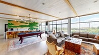Located at 947 Myers Street in Richmond, VA, this single-floor amenity lounge offers a generously proportioned gathering space designed for both relaxation and recreation. The open layout is anchored by light wood-plank flooring and exposed wood ceiling beams that run throughout, lending a warm, contemporary character to the room.

A striking living moss and wood accent wall serves as a bold focal point near the entertainment zone, where a full-size pool table sits atop a vibrant patterned area rug beneath modern pendant lighting. Adjacent to this is a bar-height counter with seating, ideal for socializing. A wall-mounted fireplace with a clean stone surround anchors a separate lounge area furnished with comfortable sofas and accent chairs.

Floor-to-ceiling windows line an entire wall of the space, flooding the interior with natural light and offering expansive views of the surrounding waterway and outdoor terrace, which features a fire pit and additional seating. A private office or leasing area is tucked toward the rear, appointed with decorative wallpaper, wood-toned furniture, and direct glass-door access to the main lounge. The overall ambiance is modern yet inviting, seamlessly blending indoor comfort with an appreciation for the scenic Richmond surroundings.