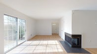 This single-floor home offers a clean, modern aesthetic throughout its well-designed layout. The expansive living room serves as the heart of the home, featuring light hardwood flooring, bright white walls, and a striking corner fireplace with a dark surround and hearth. Natural light pours in through a large sliding glass door that opens to the outdoors, creating a warm and inviting atmosphere.

Adjacent to the living area, the open-concept kitchen is equipped with gray shaker-style cabinetry, dark granite countertops, and a full suite of stainless steel appliances, including a range, microwave, and dishwasher. The hardwood flooring continues seamlessly from the living area into the kitchen, reinforcing the cohesive flow of the space.

The bedrooms are carpeted for comfort and feature white walls with ample natural light from single-pane windows offering views of the surrounding greenery. One bedroom includes direct access to a bathroom and a closet, functioning as a primary suite.

The home includes two full bathrooms. One features gray cabinetry with white countertops and a combination tub/shower, while the other offers a standalone walk-in shower with clean white surround panels and brushed nickel fixtures. Both bathrooms maintain a consistent, neutral aesthetic that complements the rest of the home.