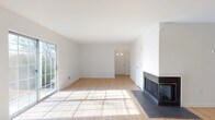 This single-floor home offers a clean, modern aesthetic throughout its well-designed layout. The expansive living room serves as the heart of the home, featuring light hardwood flooring, bright white walls, and a striking corner fireplace with a dark surround and hearth. Natural light pours in through a large sliding glass door that opens to the outdoors, creating a warm and inviting atmosphere.

Adjacent to the living area, the open-concept kitchen is equipped with gray shaker-style cabinetry, dark granite countertops, and a full suite of stainless steel appliances, including a range, microwave, and dishwasher. The hardwood flooring continues seamlessly from the living area into the kitchen, reinforcing the cohesive flow of the space.

The bedrooms are carpeted for comfort and feature white walls with ample natural light from single-pane windows offering views of the surrounding greenery. One bedroom includes direct access to a bathroom and a closet, functioning as a primary suite.

The home includes two full bathrooms. One features gray cabinetry with white countertops and a combination tub/shower, while the other offers a standalone walk-in shower with clean white surround panels and brushed nickel fixtures. Both bathrooms maintain a consistent, neutral aesthetic that complements the rest of the home.