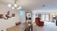 This single-floor residence offers a practical and comfortable layout across several well-defined living spaces. The living room is a welcoming area finished with plush carpeting and features a sliding glass door that fills the room with natural light. The dining area is positioned adjacent to the living room, complete with a wood dining table and an elegant multi-arm chandelier overhead, with easy access to the kitchen through a connecting hallway. The kitchen is well-equipped with warm oak cabinetry, ample counter space, a double sink, and white appliances including a range, microwave, dishwasher, and refrigerator, all set on light-toned flooring. A dedicated home office provides a quiet workspace, featuring carpeted floors, a window with blinds for natural light, and a built-in closet with a solid oak door. The bedroom is generously sized with carpet flooring and includes a large sliding-door closet for storage. Two bathrooms serve the residence — one features a single-sink vanity with an oak cabinet base and a large mirror, while the second offers a walk-in glass-door shower, a toilet, and a vanity, both finished in neutral tones with clean, simple fixtures throughout. Warm oak trim accents are consistent throughout the space, lending a cohesive and classic character to the home.