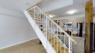 This two-floor space is designed with a clean, contemporary aesthetic that balances functionality and modern style. At the heart of the lower level, an open-concept layout connects the main living area to a well-equipped kitchen. The kitchen features warm wood-toned cabinetry, a subway tile backsplash, granite or stone countertops, a stainless steel sink, and built-in appliances including a microwave and range, providing a cohesive and practical cooking environment.

A striking staircase serves as a central architectural feature, constructed with natural wood treads and crisp white metal railings with a wood-capped handrail. The open-riser staircase design adds a sense of visual lightness and allows sightlines to flow freely between floors. Polished concrete flooring on the lower level contributes to the industrial-modern character of the space, while recessed and flush-mount ceiling lighting provides consistent illumination throughout.

The entry area is clean and functional, featuring a keypad-secured door that opens directly into the main living space. The white walls and neutral palette throughout create a bright, airy atmosphere. The overall design emphasizes an efficient use of space across both floors, with thoughtful material choices that lend the interior a refined, urban character.