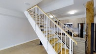 This two-floor space is designed with a clean, contemporary aesthetic that balances functionality and modern style. At the heart of the lower level, an open-concept layout connects the main living area to a well-equipped kitchen. The kitchen features warm wood-toned cabinetry, a subway tile backsplash, granite or stone countertops, a stainless steel sink, and built-in appliances including a microwave and range, providing a cohesive and practical cooking environment.

A striking staircase serves as a central architectural feature, constructed with natural wood treads and crisp white metal railings with a wood-capped handrail. The open-riser staircase design adds a sense of visual lightness and allows sightlines to flow freely between floors. Polished concrete flooring on the lower level contributes to the industrial-modern character of the space, while recessed and flush-mount ceiling lighting provides consistent illumination throughout.

The entry area is clean and functional, featuring a keypad-secured door that opens directly into the main living space. The white walls and neutral palette throughout create a bright, airy atmosphere. The overall design emphasizes an efficient use of space across both floors, with thoughtful material choices that lend the interior a refined, urban character.