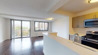 This single-floor residence is defined by rich, dark hardwood flooring that flows consistently throughout the living spaces, lending a warm and cohesive aesthetic. The open-concept layout connects the kitchen directly to the living area, creating a spacious and functional environment. The galley-style kitchen is well-appointed with stainless steel appliances, including a gas range, microwave, and refrigerator, complemented by contemporary light wood cabinetry and clean white countertops. A peninsula counter separates the kitchen from the living space, offering both additional prep area and a natural transition point between the two zones.

The living area is generously proportioned and bathed in natural light from large windows and a sliding glass door that opens to a private balcony with open city and treetop views. The bedrooms are each equipped with ceiling fans and sizable closets, including a walk-in closet accessible through bi-fold doors in one of the rooms. The bathrooms feature clean white tile work, with one room containing a full soaking tub and another offering a separate walk-in shower with modern chrome fixtures. A coat closet near the entry adds practical storage to this well-designed space.