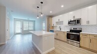 Located at 5236 Legendary Loop in Wesley Chapel, FL, this well-appointed 2-bedroom, 2-bathroom residence offers a thoughtfully designed single-floor layout. The open-concept kitchen and living area serves as the heart of the home, featuring a large central island with quartz countertops, dual pendant globe lights, and a herringbone tile backsplash. Cabinetry blends white upper cabinets with warm natural wood lower cabinets, complemented by matte black hardware. Stainless steel appliances, including a refrigerator, range, microwave, and dishwasher, complete the kitchen. Light wood-tone luxury vinyl plank flooring flows seamlessly throughout the entire residence. The living area receives generous natural light through large windows with horizontal blinds, and includes a built-in shelving nook. Both bedrooms are well-sized and bright, each featuring windows with outdoor views. The primary bathroom offers a tub-shower combo with marble-style tile surround, a wood-tone vanity with white quartz counters, and a large mirror. The second bathroom features a double vanity with matching wood cabinetry, a glass-door shower, and consistent matte black fixtures. Two closets and a hallway round out the functional layout of this clean, modern residence.