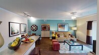 Located at 10741 W El Cortez Pl in Peoria, Arizona, this single-story residence offers a thoughtfully designed layout with a warm, contemporary aesthetic throughout. The open-concept living and dining area serves as the heart of the home, featuring rich hardwood-style flooring, crown molding, and a ceiling fan. A bold teal accent wall adds a pop of color to the living space, which is bathed in natural light from a large sliding glass door. The adjoining dining area is defined by track lighting and two-tone walls, creating a welcoming atmosphere for entertaining. The kitchen is outfitted with dark espresso cabinetry, light countertops, and a full suite of black appliances including a refrigerator, range, and built-in microwave, complemented by hardwood-style flooring and ample cabinet storage. Two bedrooms provide comfortable retreats; one features a rich golden-brown accent wall, plush carpeting, and a ceiling fan, while the second bedroom benefits from generous natural light through a large window. The full bathroom includes a tub-shower combination and hardwood-style flooring. Completing the home is a dedicated in-unit laundry area with a full-size washer and dryer and a built-in shelf for added storage convenience.