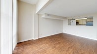 This single-floor unit offers a well-organized layout that efficiently connects its living, kitchen, bedroom, and bathroom spaces. The living area is a generous, open room finished with warm, rustic hardwood flooring that runs throughout much of the unit. A structural soffit with integrated HVAC venting adds architectural definition to the space, while floor-to-ceiling sliding glass doors dressed with vertical blinds frame sweeping elevated city views, filling the room with natural light.

A narrow, efficiently designed galley kitchen features wood-tone cabinetry, light countertops, a stainless steel double sink, and a black electric range with overhead ventilation. A separate storage or utility room is accessible directly from the kitchen. The hallway connecting the living space to the private areas is finished with wood-look flooring and provides access to both the bedroom and bathroom.

The bedroom is carpeted in neutral tones and features a high horizontal window that admits natural light while maintaining privacy. The full bathroom includes a tiled tub-shower combination, a toilet, a vanity with a wide mirror, and wood-style flooring, presenting a clean and functional finish throughout.