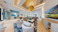 Located at 100 Windflower Ln in Daytona Beach, FL, this beautifully designed single-floor community space exudes a bright, coastal aesthetic throughout. The welcoming lobby greets visitors with light hardwood-style flooring, a statement chandelier, and large black-framed glass doors that flood the space with natural light and offer views of the surrounding landscape.

The open living lounge area features coffered and tray ceilings with warm ambient lighting, shiplap accent walls, woven rattan furnishings, and a shuffleboard table — ideal for relaxation and socializing. A kitchenette area showcases a striking teal herringbone tile backsplash, a turquoise painted ceiling, open shelving, a large island with bar seating, and pendant lighting, creating a functional yet stylish gathering hub.

Two conference rooms serve as dedicated meeting spaces, each outfitted with a large wooden conference table, teal upholstered chairs, wall-mounted displays, and abundant natural light streaming through multiple windows with lush Florida greenery views. Two intimate dining rooms provide quieter settings with round tables and soft seating, connected by frosted glass doors. Curated coastal artwork is displayed throughout, tying together the space's cohesive, resort-inspired design.