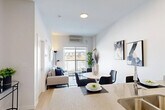 This thoughtfully designed one-bedroom, one-bathroom unit in Edmonton's southwest is arranged across a single floor, offering an efficient and well-organized layout. Light wood flooring runs throughout, lending warmth and visual continuity to the space.

The living room is bright and inviting, anchored by large windows and a balcony-facing sliding door that frames open views of the surrounding neighbourhood and fills the room with natural light. The kitchen is galley-style, featuring stainless steel appliances including a refrigerator, electric range, and over-the-range microwave, complemented by white cabinetry, stone-look countertops, and a grey tile backsplash.

The bedroom is a calm, neutral-toned retreat with a sizeable window overlooking the balcony and the broader cityscape beyond, providing natural light and an open feel. A dedicated closet and hallway offer practical storage and circulation between rooms.

The bathroom is finished with a white vanity topped with stone-look countertops, a full soaker tub with a grey tile surround extending to the ceiling, and the same light wood-style flooring found throughout the unit. The overall design palette is clean and contemporary, emphasizing neutral tones, modern fixtures, and functional use of space.