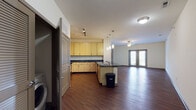 This single-story unit showcases a thoughtfully designed open-concept layout where the kitchen and living area flow seamlessly together. Rich, dark hardwood flooring extends throughout the main living spaces, creating a warm and cohesive aesthetic. The kitchen is well-appointed with light wood cabinetry, dark countertops, and a full suite of stainless steel appliances, including a refrigerator, range, microwave, and dishwasher. A central island with pendant lighting above provides additional prep space and a natural division between the kitchen and living area. The spacious living room is anchored by a ceiling fan and benefits from natural light streaming through a set of French doors that open to an outdoor area. Neutral white walls throughout create a clean, versatile backdrop. The bedrooms feature plush carpeting, ceiling fans, windows with outdoor views, and walk-in closets with built-in hanging rods. The bathroom is finished with slate-toned tile flooring, a full soaking tub, tile surround, and a curved shower rod, complemented by a vanity with warm wood cabinetry.
