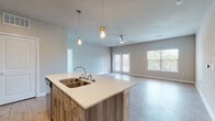 This well-appointed single-floor residence offers a thoughtfully designed open-concept layout that seamlessly connects the kitchen and living areas. The kitchen is a standout feature, showcasing light wood cabinetry, white quartz countertops, a central island with a double-basin sink, stainless steel appliances — including a range, microwave, and refrigerator — and a subtle tile backsplash. Stylish gold-accented pendant lights hang above the island, adding a modern touch. The living area extends naturally from the kitchen, featuring durable wood-look flooring, a ceiling fan, and generous natural light from large windows and glass French doors that offer outdoor views. The bedrooms are carpeted for comfort, with neutral-toned walls and ample natural light provided by multiple windows with blinds. The bathrooms are finished with the same light wood cabinetry and quartz countertops found in the kitchen, complemented by wood-look vinyl flooring. One bathroom features a walk-in glass shower, while another includes a full tub and shower combination. Throughout the space, a cohesive neutral color palette and contemporary finishes create a clean, modern ambiance.