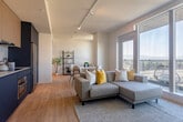 Located in San Jose, CA, this thoughtfully designed 2-bedroom, 3-bathroom residence offers a modern open-concept layout with light wood flooring throughout and a clean, contemporary aesthetic. The living room is a bright, inviting space anchored by floor-to-ceiling windows and a sliding glass door that opens to a private balcony, offering stunning panoramic views of the San Jose cityscape and distant mountains. The kitchen features striking two-tone cabinetry — bold navy blue lower cabinets paired with natural wood upper cabinets — complemented by a white tile backsplash, sleek countertops, and stainless steel appliances including a built-in oven and refrigerator. Two well-appointed hallways connect the living areas to the bedrooms, with one hallway showcasing large-scale wall art, adding an artistic touch to the space. The primary bedroom is a comfortable retreat with warm, neutral tones and ample natural light. The second bedroom is equally well-sized with a clean, minimalist design. All three bathrooms are finished with neutral mosaic tile, walk-in showers with frosted glass enclosures, floating vanities, and backlit mirrors, creating a spa-like atmosphere throughout.