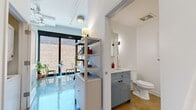 Located at 5060 N Broadway Street in Chicago's vibrant Uptown neighborhood, this single-floor studio unit offers a thoughtfully designed layout with a modern, minimalist aesthetic. The space is defined by polished concrete floors that run throughout, reflecting natural light and lending an industrial-chic character to the interior.

The main living area is anchored by large, floor-to-ceiling windows with black frames that face an adjacent brick building, allowing generous natural light to fill the space. The open layout accommodates a sleeping area, a seating and dining zone, and easy access to other functional areas. Tall ceilings, visible structural elements, and a wall-mounted split AC unit add to the loft-inspired feel.

The kitchen is compact and efficiently arranged, featuring soft blue-grey cabinetry, white subway tile backsplash, open wooden shelving, a gas range, and full-size refrigerator. The bathroom is cleanly finished with matching blue-grey vanity cabinetry, a white countertop, and a glass-enclosed walk-in shower with white tile surround and matte black hardware. A wooden bath mat and framed artwork complete the polished look.

An open shelving unit serves as a subtle room divider between the sleeping and entry areas, adding storage while maintaining visual flow throughout the unit.